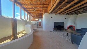A spacious living area with a large TV, a fireplace, and a view of the sky through the windows. - Unique Baja Earthship, in the desert with views of the sea and mountains (San Felipe)