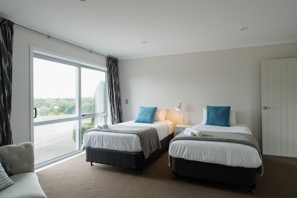 A hotel room with two beds, a sofa, and a large window with curtains. - The Wine Country Retreat by Homello (Kumeū)