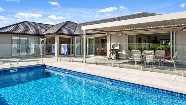 Una piscina con solárium empedrado, mobiliario exterior y un patio cubierto.