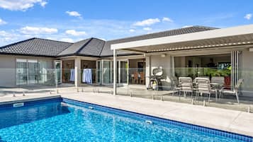 Una piscina con solárium empedrado, mobiliario exterior y un patio cubierto.