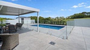 Un espacio al aire libre techado con piscina, mobiliario y un pérgola.