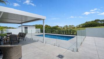 Un espacio al aire libre techado con piscina, mobiliario y un pérgola.