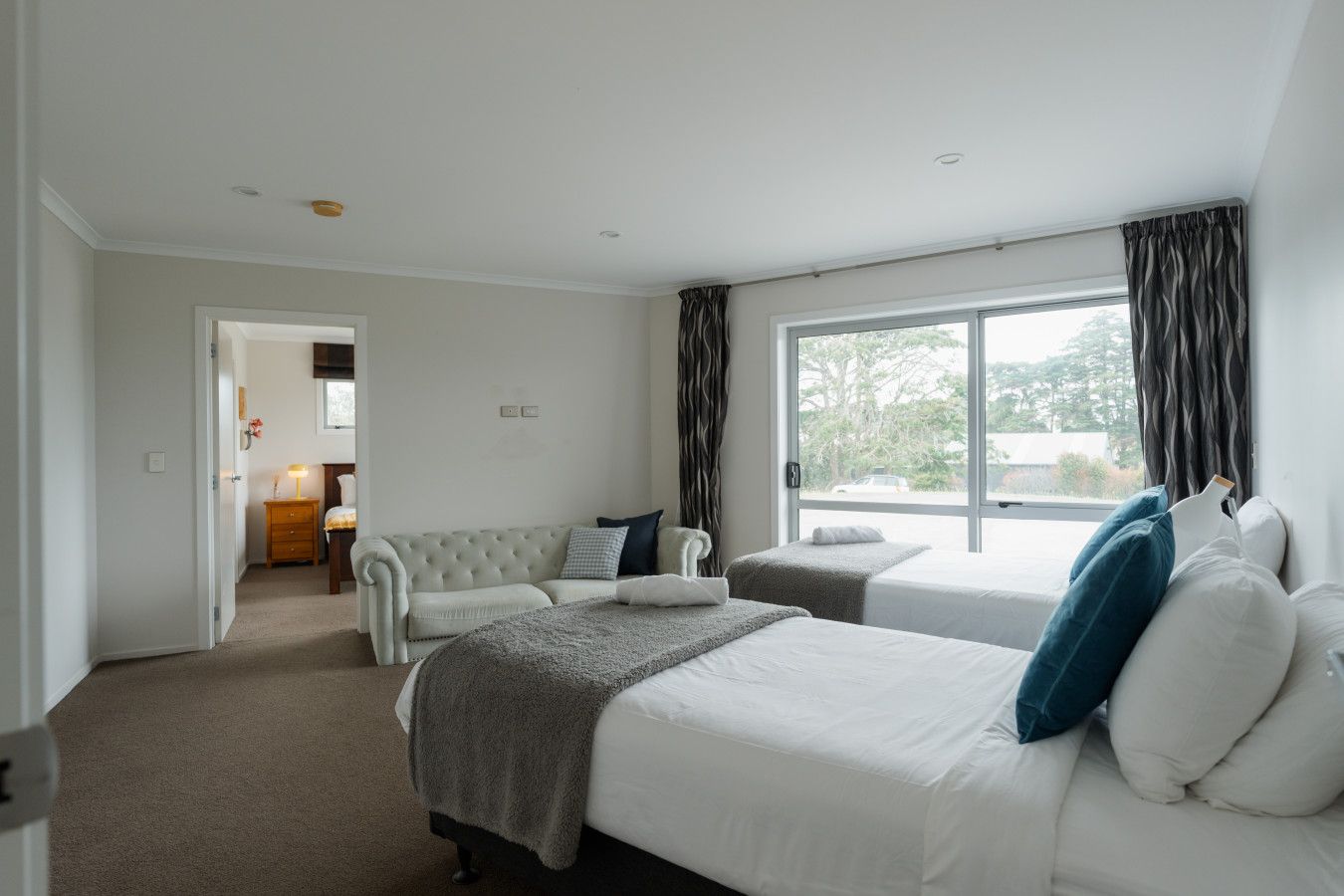 Habitación de hotel con dos camas, un sofá, una ventana con cortinas y vistas al exterior.