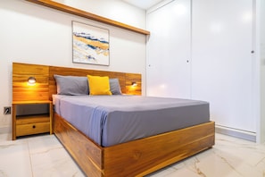 Ein modernes Schlafzimmer mit einem hölzernen Kopfteil, einem Bett mit grauer Bettwäsche, zwei Nachttischlampen, einem Nachttisch und einem großen Fenster.