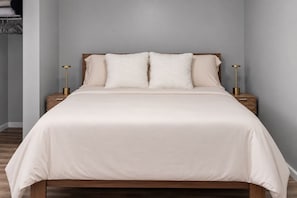A bed with a wooden frame and a white bedspread, flanked by two bedside tables with lamps.
