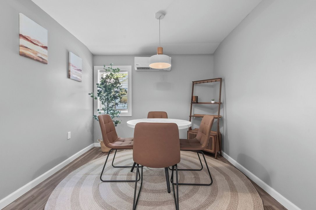 A dining area with a round table, four chairs, a hanging light fixture, and a bookshelf.