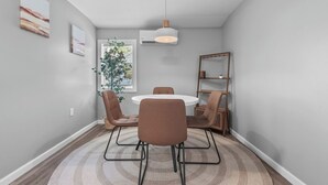 A dining area with a round table, four chairs, a hanging light fixture, and a bookshelf. - The Howder House / Refined 1BR  / Sleeps 4 (Hillsdale)