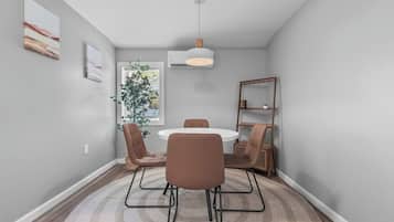 A dining area with a round table, four chairs, a hanging light fixture, and a bookshelf.