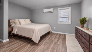 A bedroom with a bed, a dresser, an air conditioning unit, and a window with blinds. - The Howder House / Refined 1BR  / Sleeps 4 (Hillsdale)