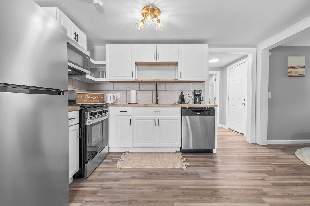 A modern kitchen with white cabinets, stainless steel appliances, and a wooden countertop.