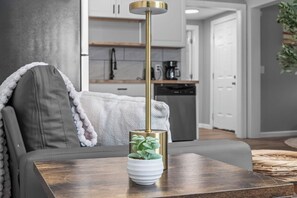 Ein modernes Wohnzimmer mit einer Couch, einem Couchtisch mit Pflanze und einer Küche im Hintergrund.