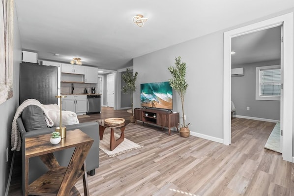 A modern living room with a flat-screen TV, a dining table, and a sofa.