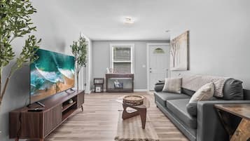 A modern living room with a flat-screen TV, a grey sofa, a coffee table, and a wooden entertainment unit.