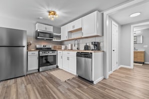 Una cocina moderna con muebles blancos, electrodomésticos de acero inoxidable y piso de madera.