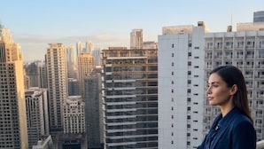 Una persona parada en un balcón con vista a un paisaje urbano de edificios altos.