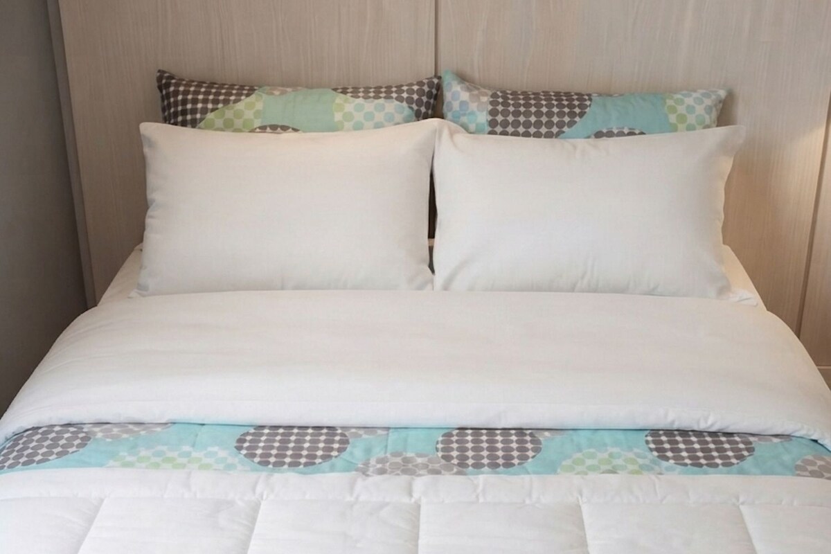 A bed with a white duvet and patterned pillows, a quilt with geometric designs, and a wooden headboard.