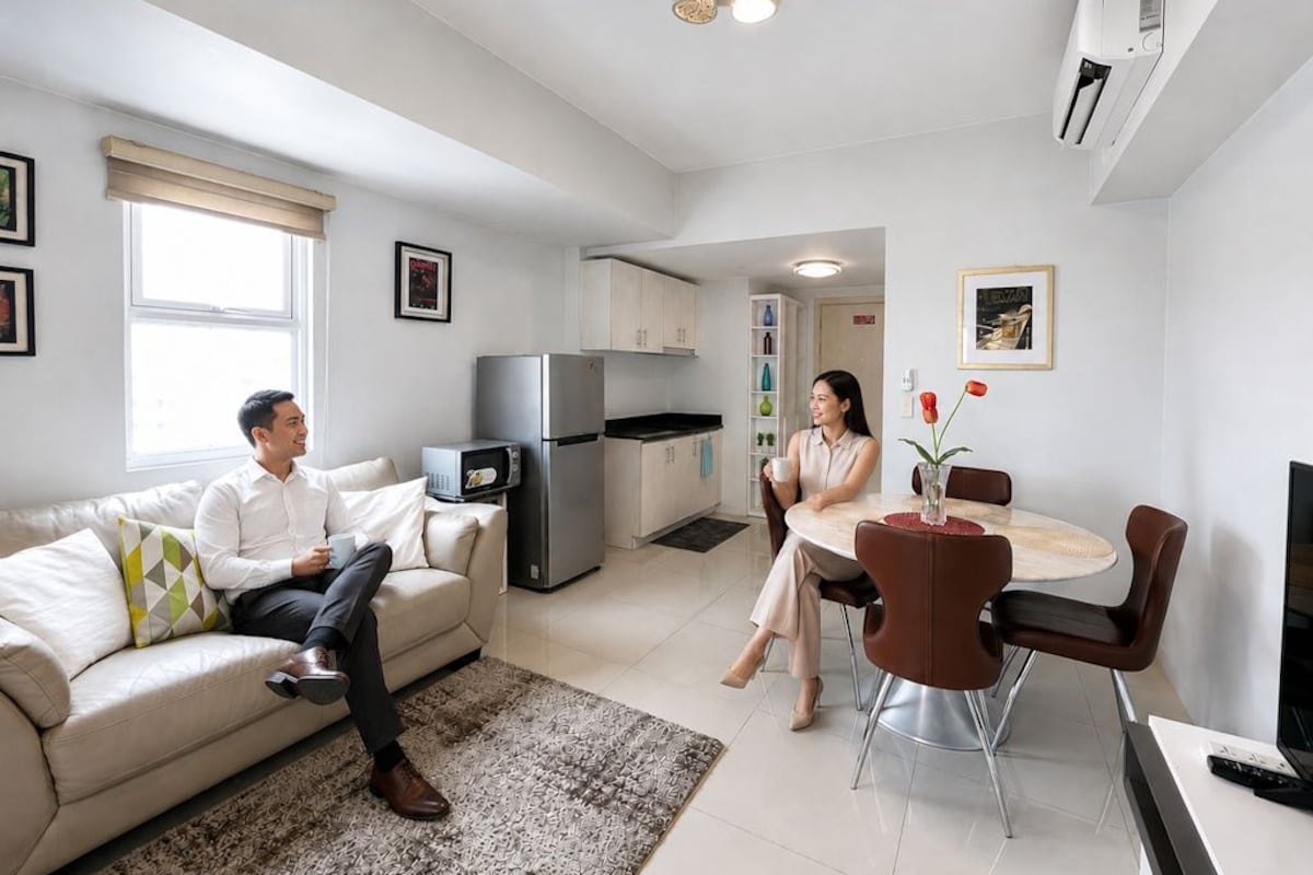 A modern living room with a sofa, a dining table with chairs, a kitchen area with a refrigerator, and a TV.