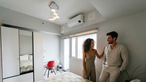 Un dormitorio con una cama, una silla roja, un espejo grande y un equipo de aire acondicionado.
