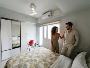 A bedroom with a bed, a red chair, a large mirror, and an air conditioning unit. - Makati CBD Executive Skyline Apartments (Makati)