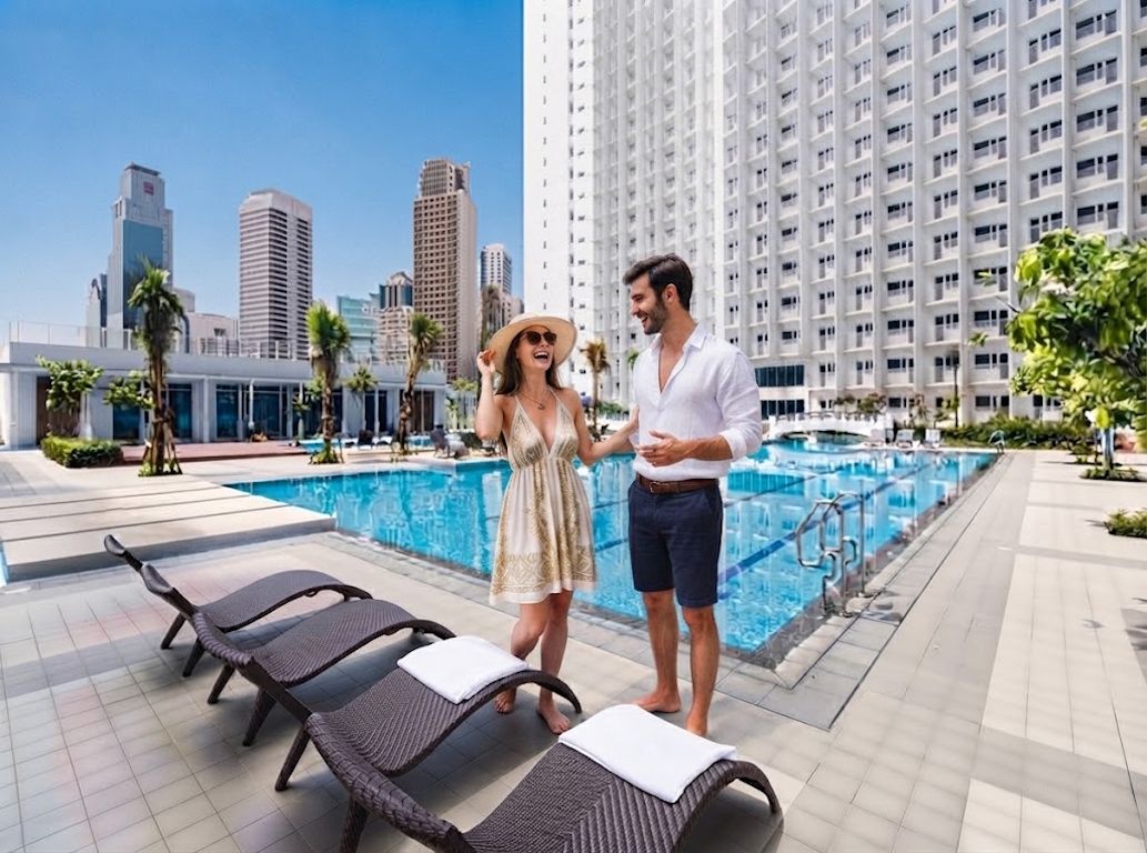 Un espace aménagé au bord de la piscine avec des chaises longues, un grand bâtiment en arrière-plan et un ciel dégagé.