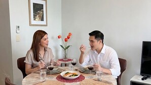 Una mesa de comedor con cubierta de mármol blanco, rodeada de sillas marrones. Hay un jarrón con flores rojas sobre la mesa, y un cuadro en la pared.