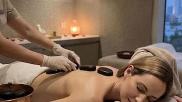 Sesión de masoterapia en un spa, con un cliente recostado en una camilla de tratamiento, un terapeuta aplicando presión con un instrumento y una vela al fondo.