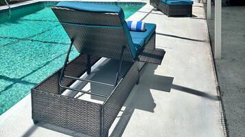 A covered outdoor swimming pool area with lounge chairs and a barbecue grill.