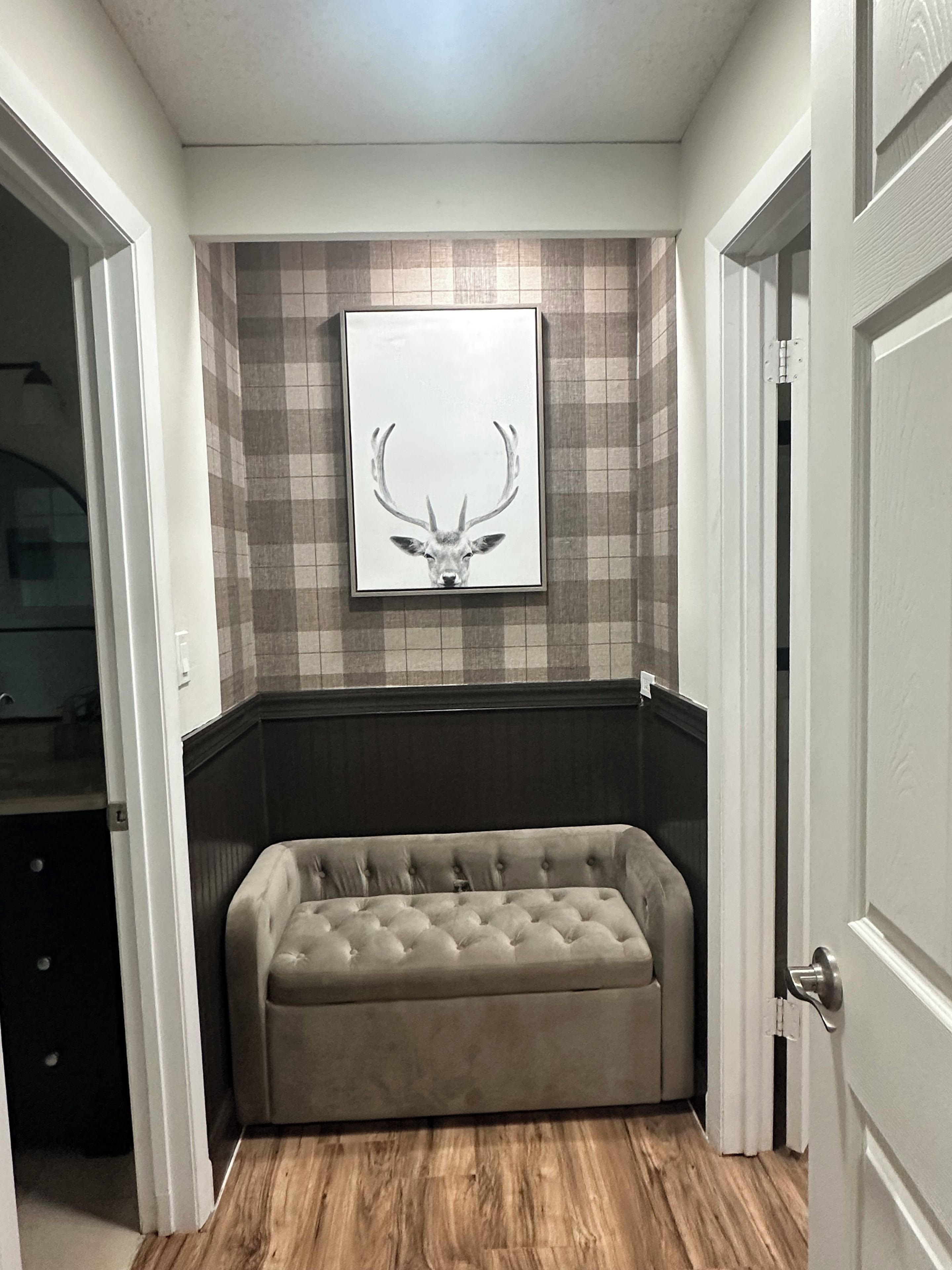 Quarto com sofá estofado, arte com cabeça de veado na parede e painel de azulejos xadrez.