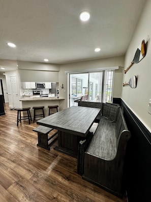 A modern kitchen with a dining area, wooden flooring, and a large window providing natural light.