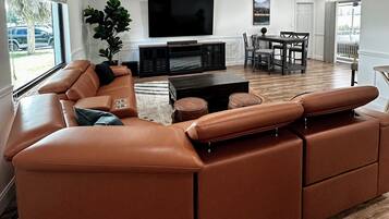 A modern living room with a large sectional sofa, a flat-screen TV, and a dining area with a table and chairs.