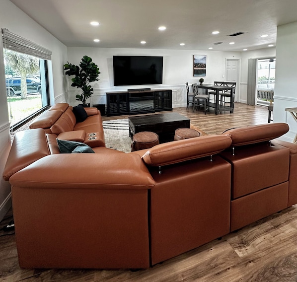 A modern living room with a large sectional sofa, a flat-screen TV, and a dining area with a table and chairs.