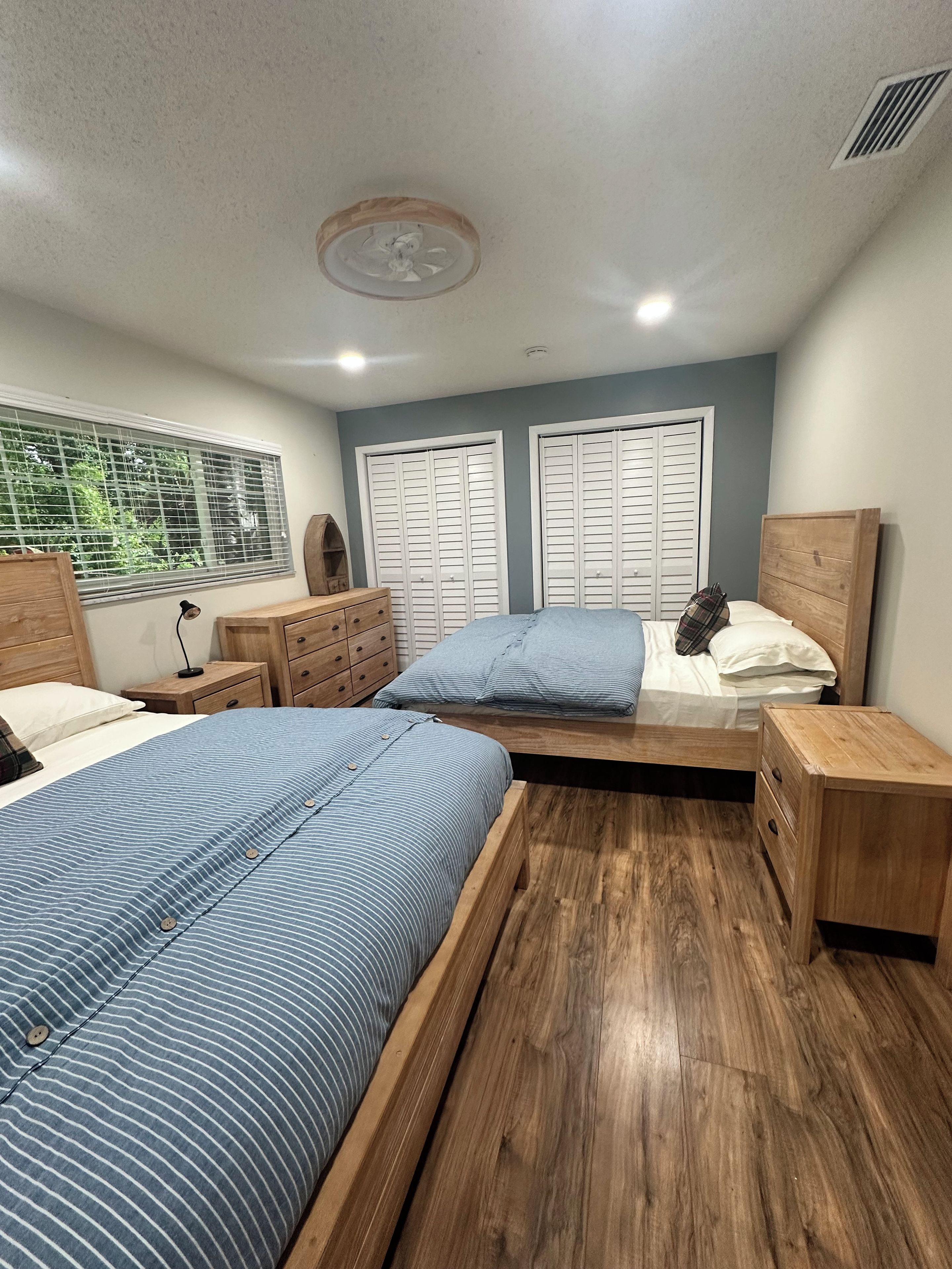 A bedroom with two beds, wooden headboards, a window with blinds, and a ceiling fan.