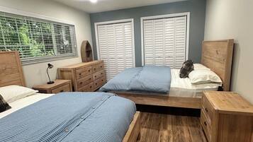 A bedroom with two beds, wooden headboards, a window with blinds, and a ceiling fan.