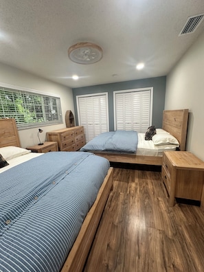A bedroom with two beds, wooden headboards, a window with blinds, and a ceiling fan.
