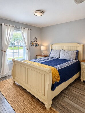 Une chambre à coucher avec un lit, une table de chevet, une lampe et une fenêtre avec des rideaux.