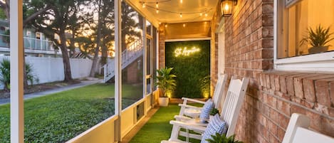 A covered outdoor seating area with artificial grass, white chairs, and string lights.