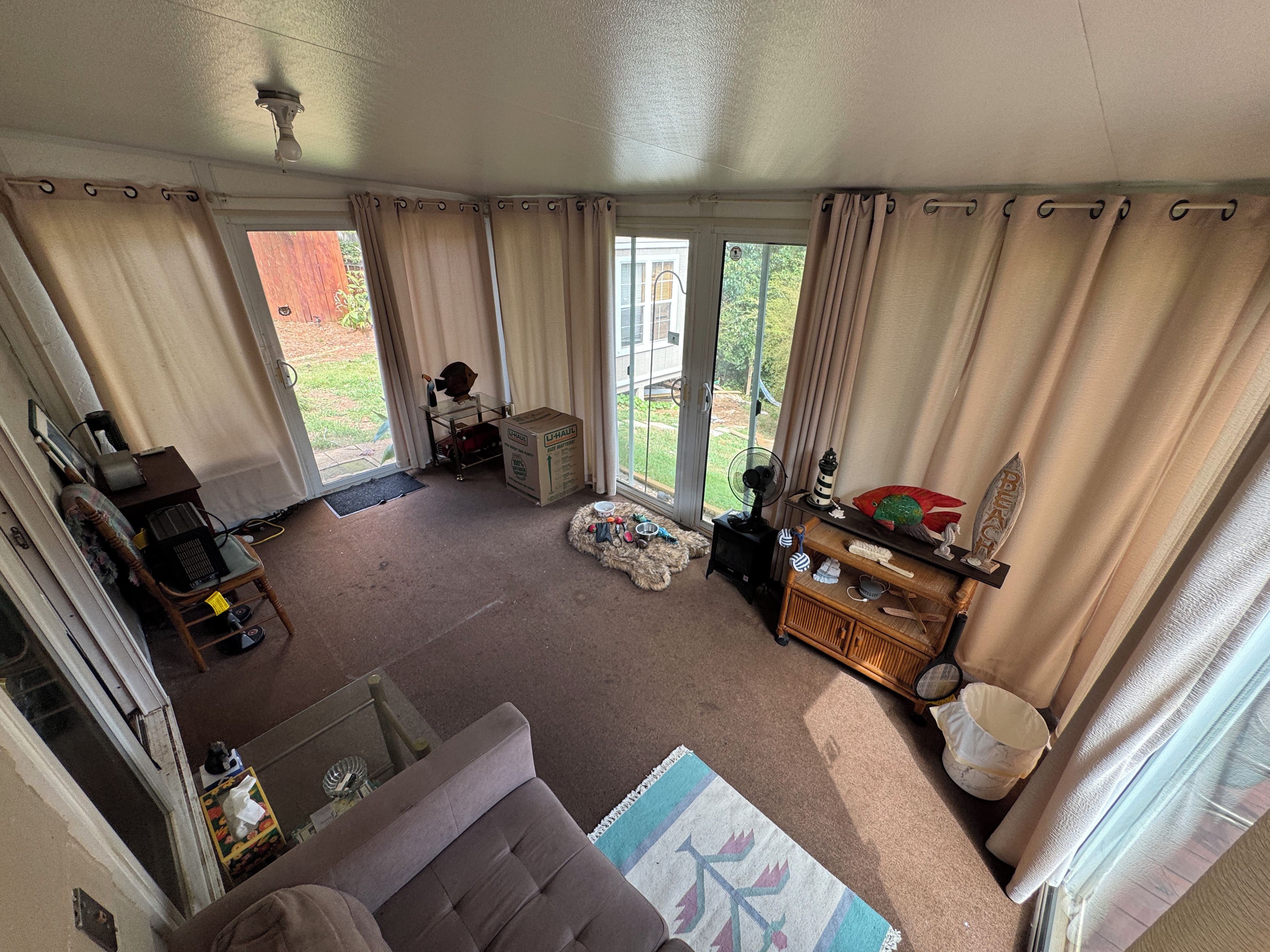 Een woonkamer met een bank, een bijzettafeltje, een ventilator en een raam met gordijnen.