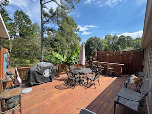 Una terraza de madera con mobiliario exterior, incluyendo una mesa, sillas y una parrilla.