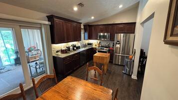 A modern kitchen with dark wood cabinets, stainless steel appliances, and a wooden dining table with chairs.