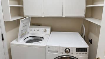 Een wasruimte met een voorlader wasmachine en droger, witte kasten erboven en een zwarte deurmat.