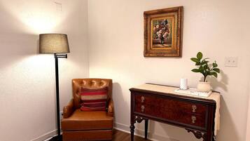A room with a brown leather armchair, a floor lamp, a wooden side table with a vase and a plant, and a framed painting on the wall.