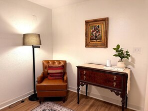 A room with a brown leather armchair, a floor lamp, a wooden side table with a vase and a plant, and a framed painting on the wall. - Nomad & Nest- Renovated Tiny Home in Historic Monte Vista (San Antonio)