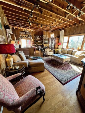 A cozy living room with wooden beams, a fireplace, and a view of the outdoors. - 1895 Cottage At Belle Knowle (Eldred)