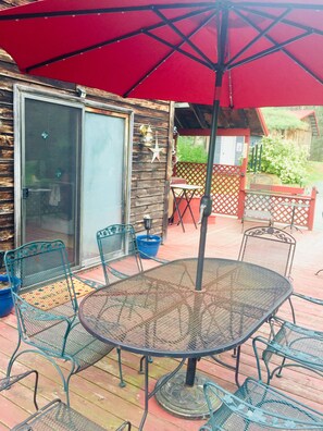 A covered patio area with a round metal table and chairs, a red umbrella, and a wooden deck. - 1895 Cottage At Belle Knowle (Eldred)