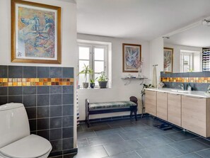 Un bagno con un water, una panca, un lavandino e due finestre.