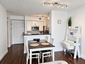 Een moderne keuken met roestvrijstalen apparatuur, een eethoek met een donker houten tafel en witte stoelen, en een witte bureaustoel.