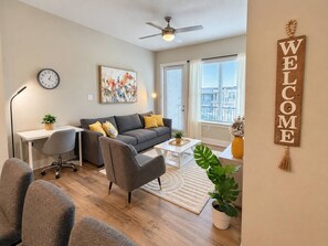 A modern living room with a grey sofa, a coffee table, a desk, and a plant. - Big Home 3 Beds Balcony Pool View Gym Downtown Jax (Jacksonville)