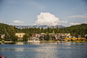 A lakeside view with a row of multi-story buildings, a dock, and a mountain backdrop. - Lakeview Condo with Private Balcony by Bigfork Bay (Bigfork)