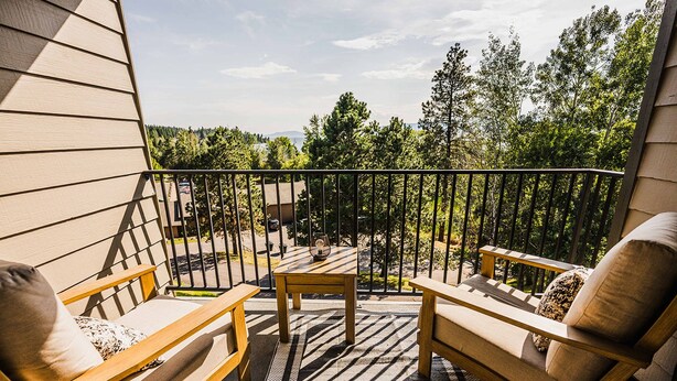 Een balkon met houten meubels, een tafeltje en uitzicht op bomen en een verafgelegen landschap.