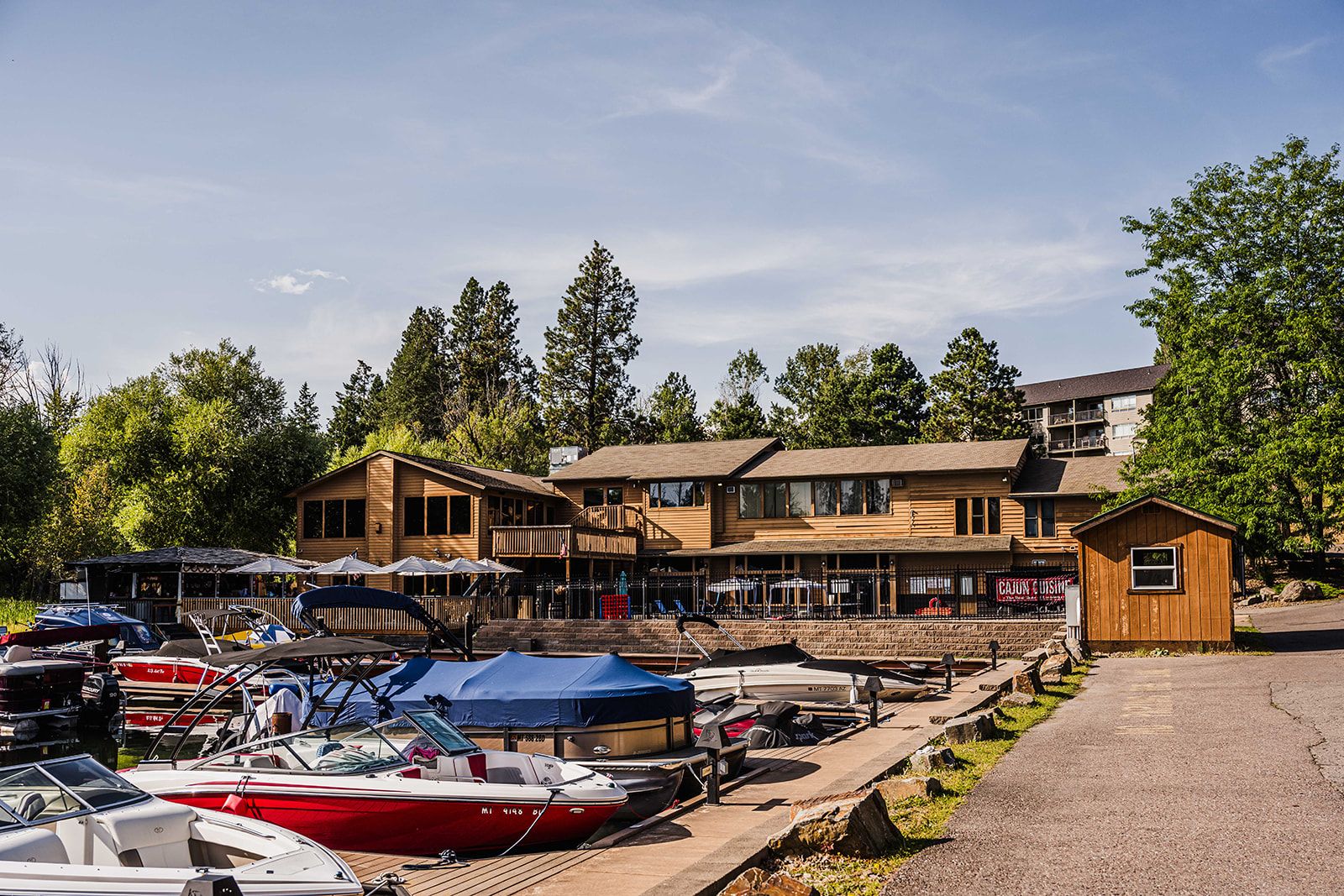 A marina with boats docked, a wooden building with a balcony, and a small shed.